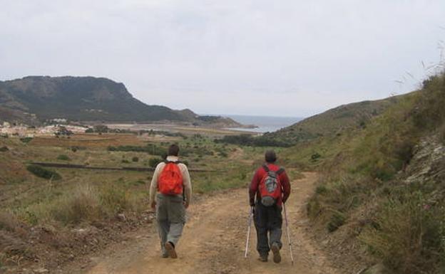 Dos senderistas caminan por el último tramo de la Carretera del 33, con la bahía de Portmán a la vista.