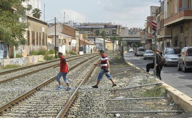 Tres ciudadanos atraviesan las vías del tren aprovechando las vallas derribadas. 