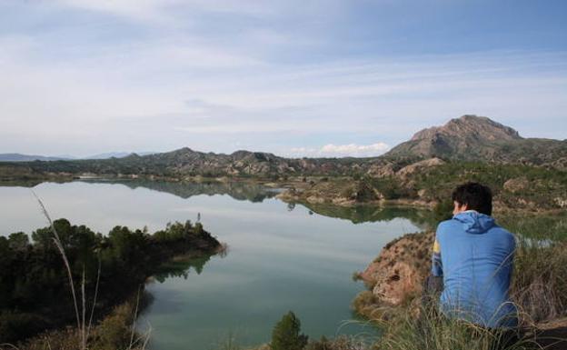 Un excursionista observa la lámina de agua del pantano de Alfonso XIII desde un montículo./