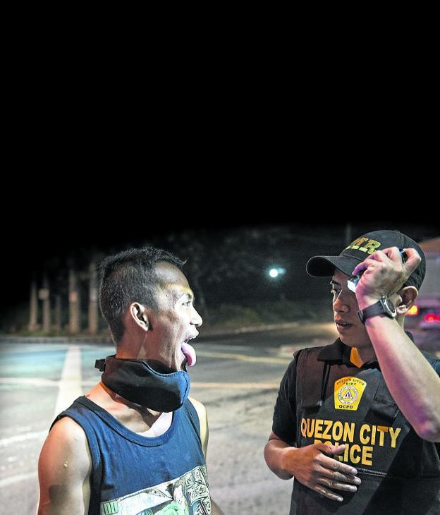 Control exhaustivo en Manila. Un agente de la Policía Nacional filipina inspecciona la boca de un sospechoso para comprobar si esconde droga en su interior./Zigor Aldama