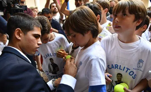 Alcaraz signs an autograph on a child's shirt.
