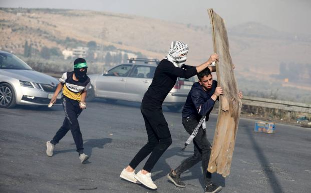 Several Palestinian civilians confront Israeli forces near Nablus, protecting themselves with a cardboard sheet.