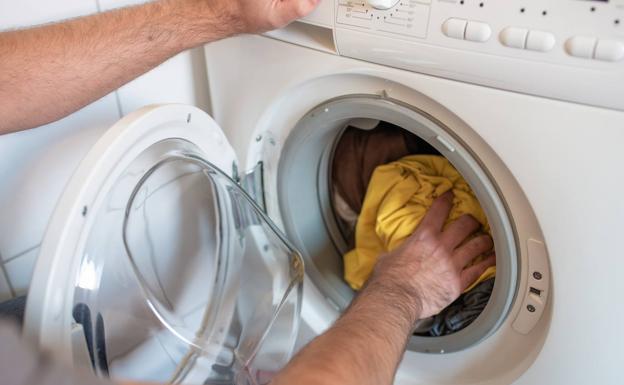A man puts clothes in the washing machine.