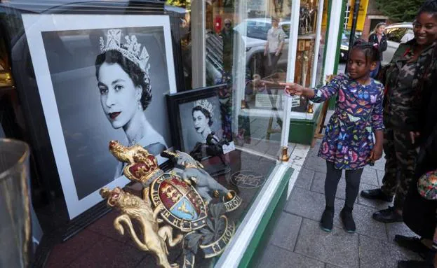 A family admires portraits of Elizabeth II in a shop window in London. 