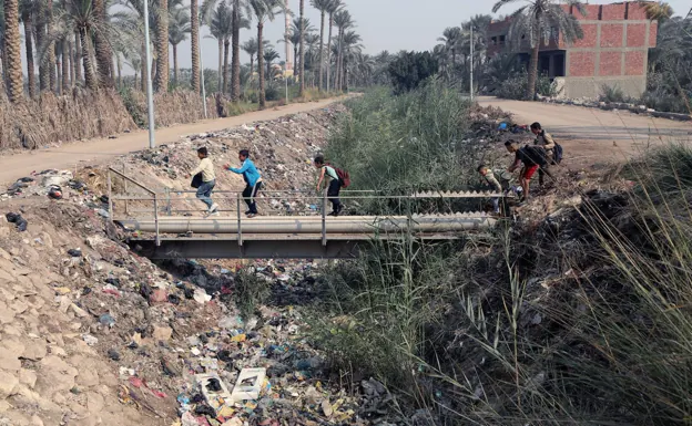 A group of children crosses a bridge over a garbage-filled river in Egypt. 