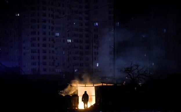 A man warms himself on a bonfire next to a building without electricity in kyiv. 