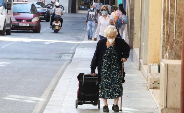 An elderly woman walks dragging a shopping cart, in a file image.